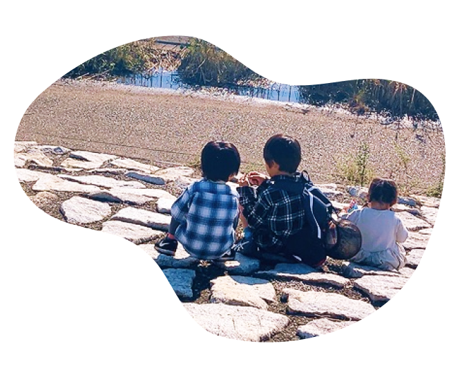 川沿いの石畳に並んで座る3人の子どもたちの後ろ姿